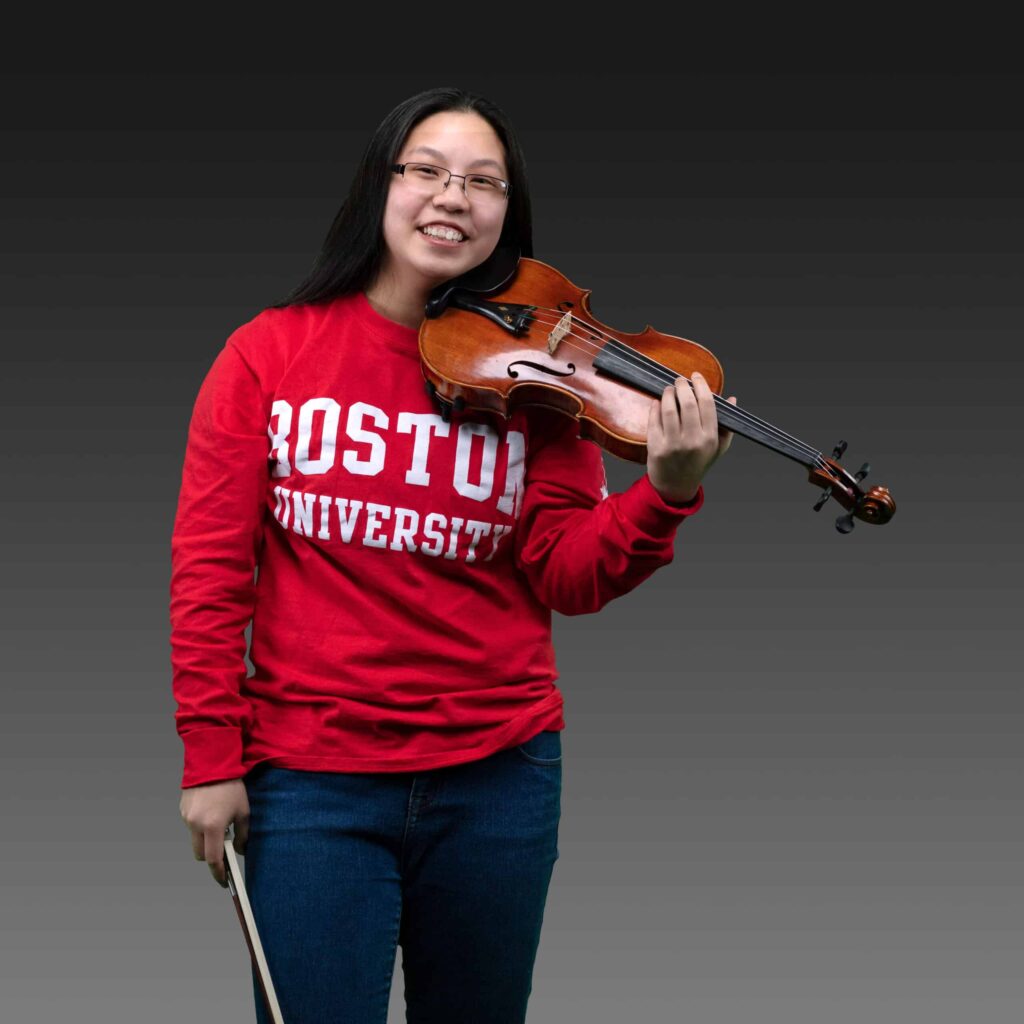 Picture of senior Erika holding a violin while wearing branded Boston University apparel